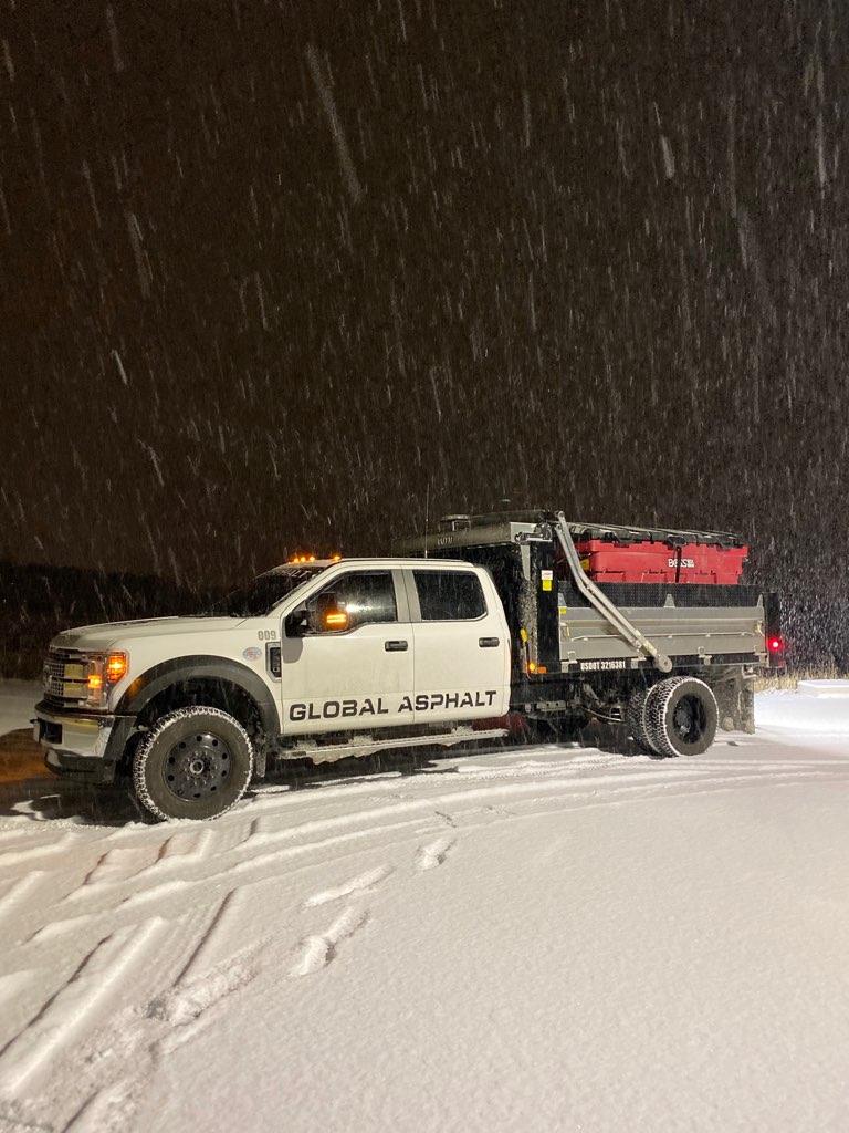 Global Asphalt salt truck with a spreader on a snowy lot at night