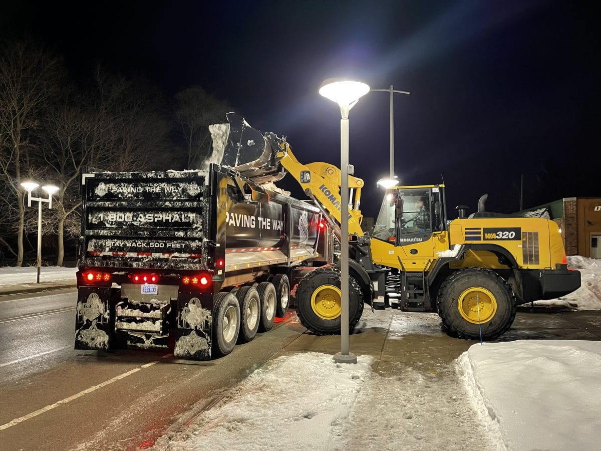 Loader filling a Global Asphalt dump truck with snow under a parking lot light